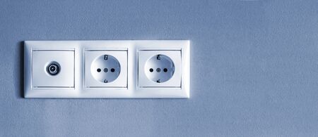electrical outlets, set of three white empty electrical sockets and antenna socket for TV with light shadow on empty grey background, electrical point of power in house, closeup, minimalism concept, banner with copy space , toning in classic blueの写真素材