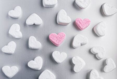 two pink marshmallow hearts lies among white sugar marshmallows in shape of hearts evenly laid out...