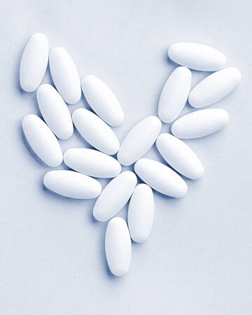 heart shaped medical white oval pills close-up isolated on classic blue background. Health treatment...