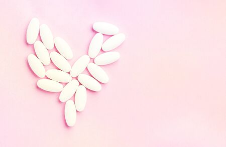 white heart from tablets and pills isolated on pink background with sunlight. Health treatment choice healthy lifestyle concept. Copy space advertisement. Medical banner with place for text.の写真素材