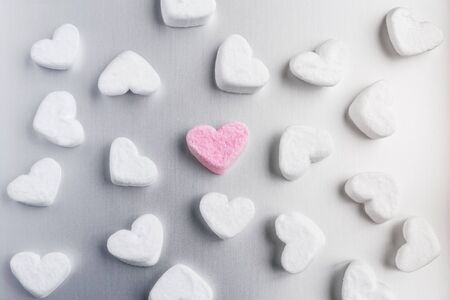 pink marshmallow heart lies among white sugar marshmallows in shape of hearts evenly laid out on a gray aluminum backgroundの写真素材