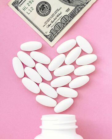 Heart made of pills and money over the neck of a bottle. Expensive medicine and venal love on pink background. Valentine's Day Pillsの写真素材