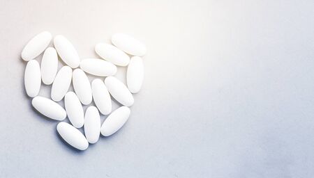 Medicine white pills, tablets and capsules for the treatment of heart disease on gray background. Pills close-up, heart disease. Medical banner, copy space, place for text.の写真素材