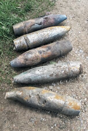 Five unexploded artillery shells lie on the side of the asphalt road, in the summer dandelions bloom and the grass turns green. War concept, rusty shells. Top viewの写真素材