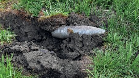 Unexploded new, brilliant artillery shell plowed and blew up the black earth on green grass. Peace and warの写真素材