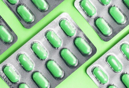 Green tablets in a blister pack, pills in foil blister packs, medications drugs on green surface. Medicines for various diseases. Top view, flat lay, tasty antidepressantの写真素材