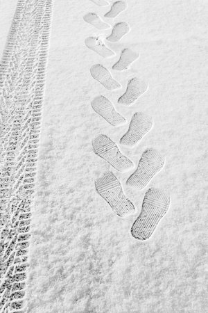 rhythmic footprint, boot tracks and car tires on thin white snow in winter go into the distance, vertical frame, ribbed tread, winter concept close-upの写真素材