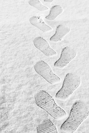 rhythmic boot prints on thin white snow in winter recede into the distance, vertical frame, ribbed protector, winter concept, close-upの写真素材