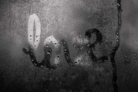 close-up inscription love by hand on wet misted glass with drips of drops, drops like tears, holiday on February 14, non-holiday mood, greeting card for Valentines day holidayの写真素材