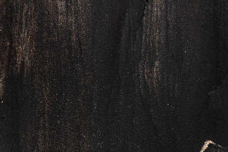 The metal texture of the background painted in black paint with smudges, scratches and splashes of gold sparklesの写真素材