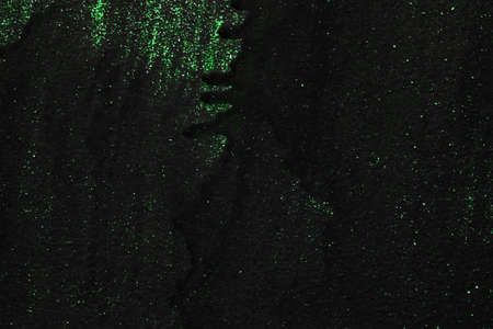 The metal texture of the background painted in black paint with smudges, scratches and splashes of green neon sparkles, new year conceptの写真素材