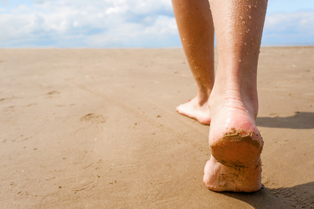 Female walking on sand beach leaving footprints in the sand. Closeup detail of female feet and golden sand.の写真素材