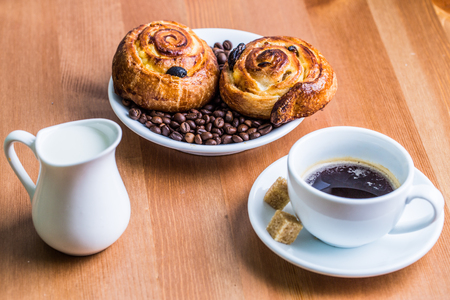 Coffee cup with cinnabon and milk jug on wooden background. Breakfast background.の写真素材