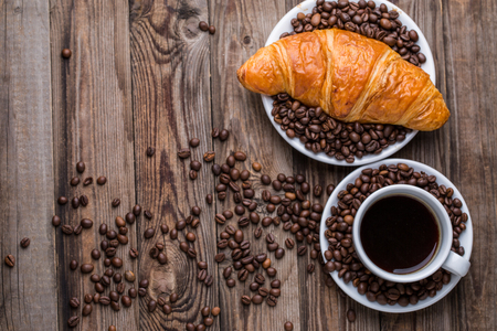 Breakfast coffee - cup and croissant with coffee beans on wooden background. Top view.の写真素材