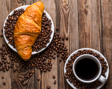 Breakfast coffee - cup and croissant with coffee beans on wooden background. Top view.の写真素材