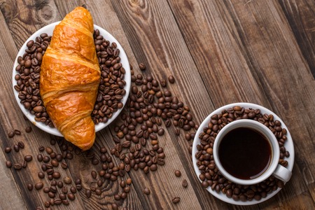 Breakfast coffee - cup and croissant with coffee beans on wooden background. Top view.の写真素材