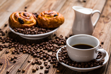 Coffee cup with milk jug and cinnabons on wooden background. Breakfast background.の写真素材