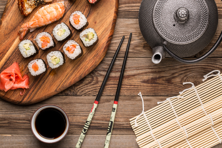 Rolls with sauce, chopsticks and teapot on wooden background, Japanese traditional foodの写真素材
