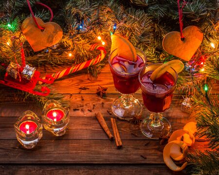 Two glasses of mulled wine with orange slices, candles and Christmas tree with garland and toys on wooden background. Christmas time.の写真素材
