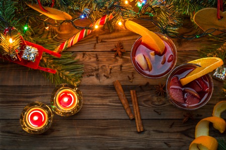 Two glasses of mulled wine with orange slices, candles and Christmas tree with garland and toys on wooden background. Christmas time. Flat layの写真素材