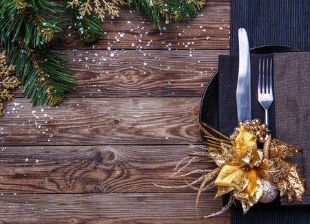 Christmas table place setting with black napkin, plate, fork and knife, decorated gold flower and christmas pine branches. Christmas holidays background.の写真素材
