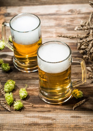 Two mugs of beer on wooden table with hops, top viewの写真素材