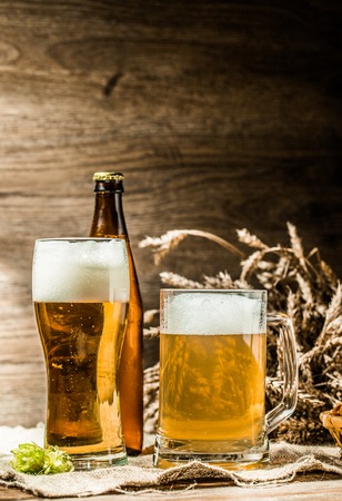 Mug, glasse, bottle of beer with foam on blank wooden background with hop, pretzels and wheatの写真素材