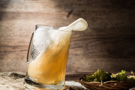 Frothy beer poured from tankard standing on linen cloth on empty wooden backgroundの写真素材