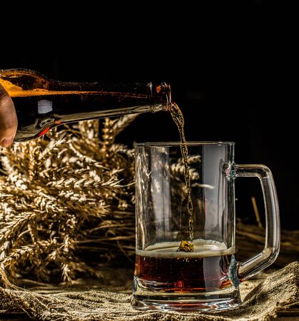 Foamy beer from bottle poured into mug standing on empty wooden backgroundの写真素材