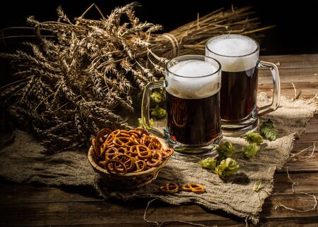 Couple beer mug with hop and pretzels on linen cloth on wooden tableの写真素材