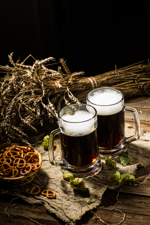 Two tankard beer with wheat and hops , basket of pretzels on wooden tableの写真素材