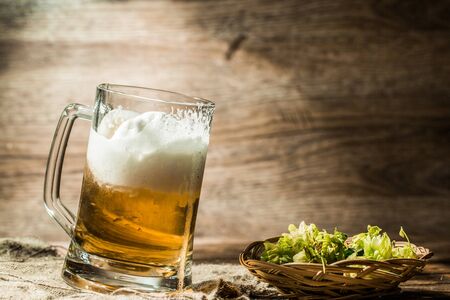 Frothy beer poured from cup standing on linen cloth on empty wooden backgroundの写真素材