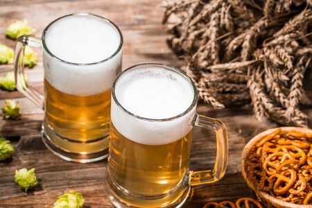 Cups with frothy beer, hops, pretzels and wheat on wooden table , top viewの写真素材