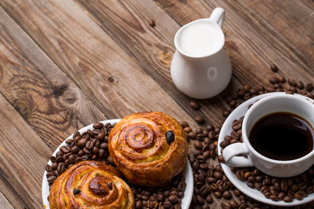 Coffee cup with milk jug and cinnabons on wooden background. Breakfast background.の写真素材