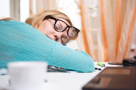 Girl student in blue sweater and glasses is sleeping on tableの写真素材