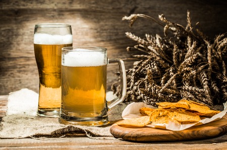 Mug, glass of beer on linen cloth with wheat spikelets and potato chipsの写真素材