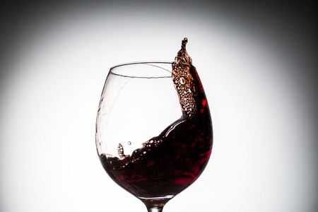 Stream of wine being pouring into a glass. Closeup splash of wine.の写真素材