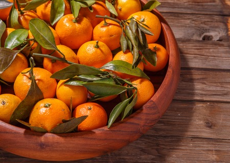 Mandarin oranges with leaves in wooden plate on rustic wood background. Winter fruits.の写真素材