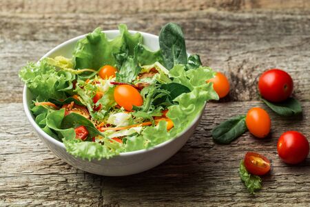 Salad with fresh vegetables - tomatoes, carrots, bell peppers and mixed greens - arugula, mesclun, mache - on wooden background.の写真素材