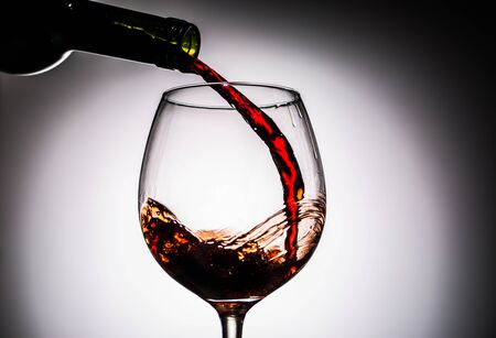 Grape wine poured from bottle into wine glass from glass on blank backgroundの写真素材