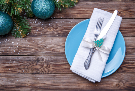 Christmas table place setting with blue plate, fork and knife, decorated ribbon and bow with fir-tree toy, white napkin and christmas pine branches with christmas balls. Christmas holidays background.の写真素材