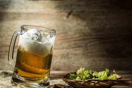Big tankard of beer standing on empty wooden background with hops on tableの写真素材