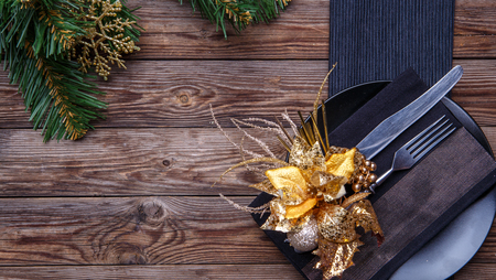 Christmas table place setting with black napkin, plate, fork and knife, decorated gold flower and christmas pine branches. Christmas holidays background.の写真素材