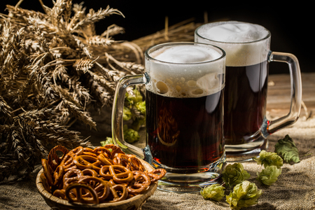 Two tankard beer with wheat and hops , basket of pretzels on wooden tableの写真素材