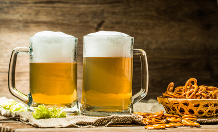 Couple beer mug with hop and pretzels on linen cloth on wooden tableの写真素材