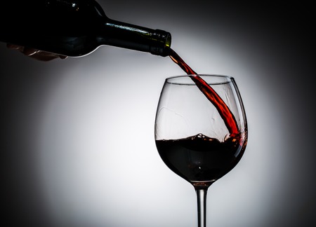 Grape wine poured from bottle into wine glass from glass on blank backgroundの写真素材
