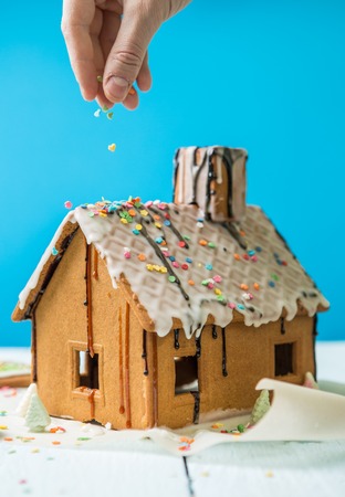 Man sprinkles Homemade gingerbread house confectionery sprinkling on blue background.の写真素材