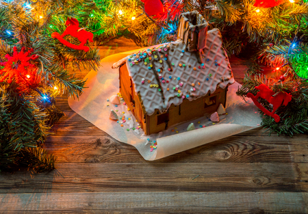 Homemade gingerbread house and christmas tree brunch with toys and garland on wooden tableの写真素材