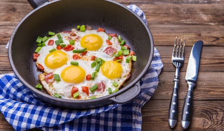 Fried eggs in pan with tomatoes and green fresh onion.の写真素材