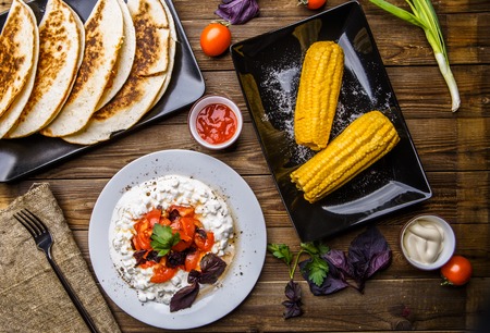 Quesadilla, salad with cottage cheese and tomatoes, two corn on wood table. Top wiev. Fresh dinner.の写真素材
